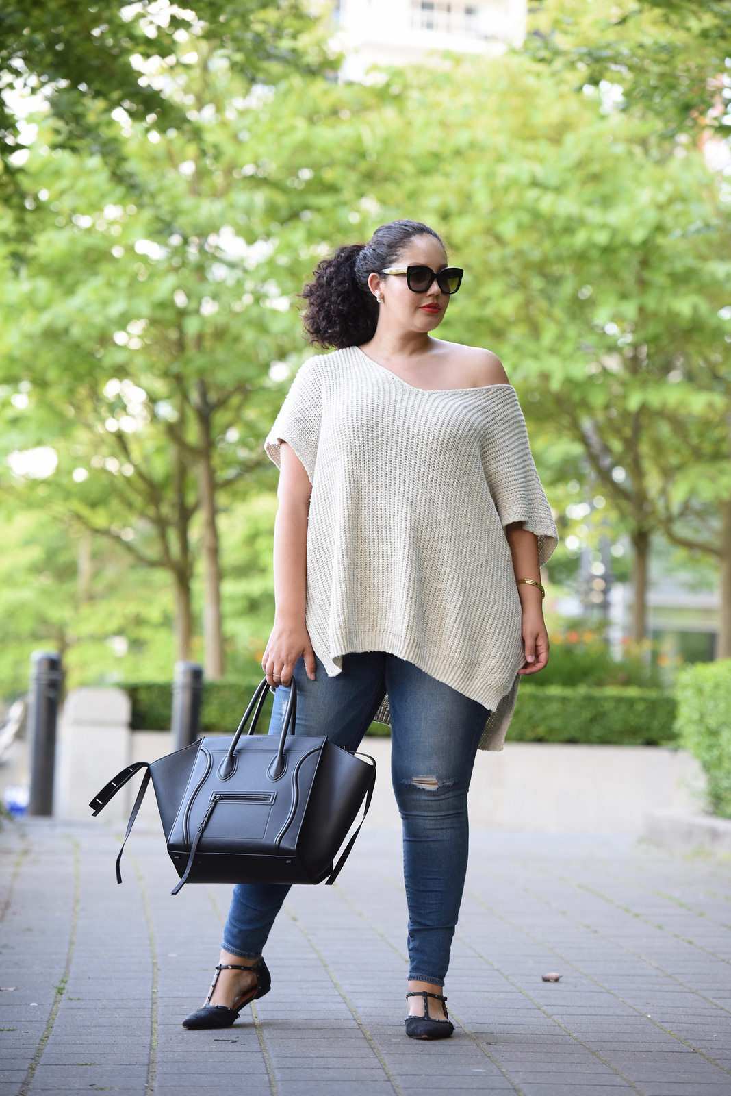 Tanesha Awasthi (formerly known as Girl with Curves) wearing an off the shoulder sweater, distressed jeans, flats and Celine Phantom bag at the park in downtown Vancouver.