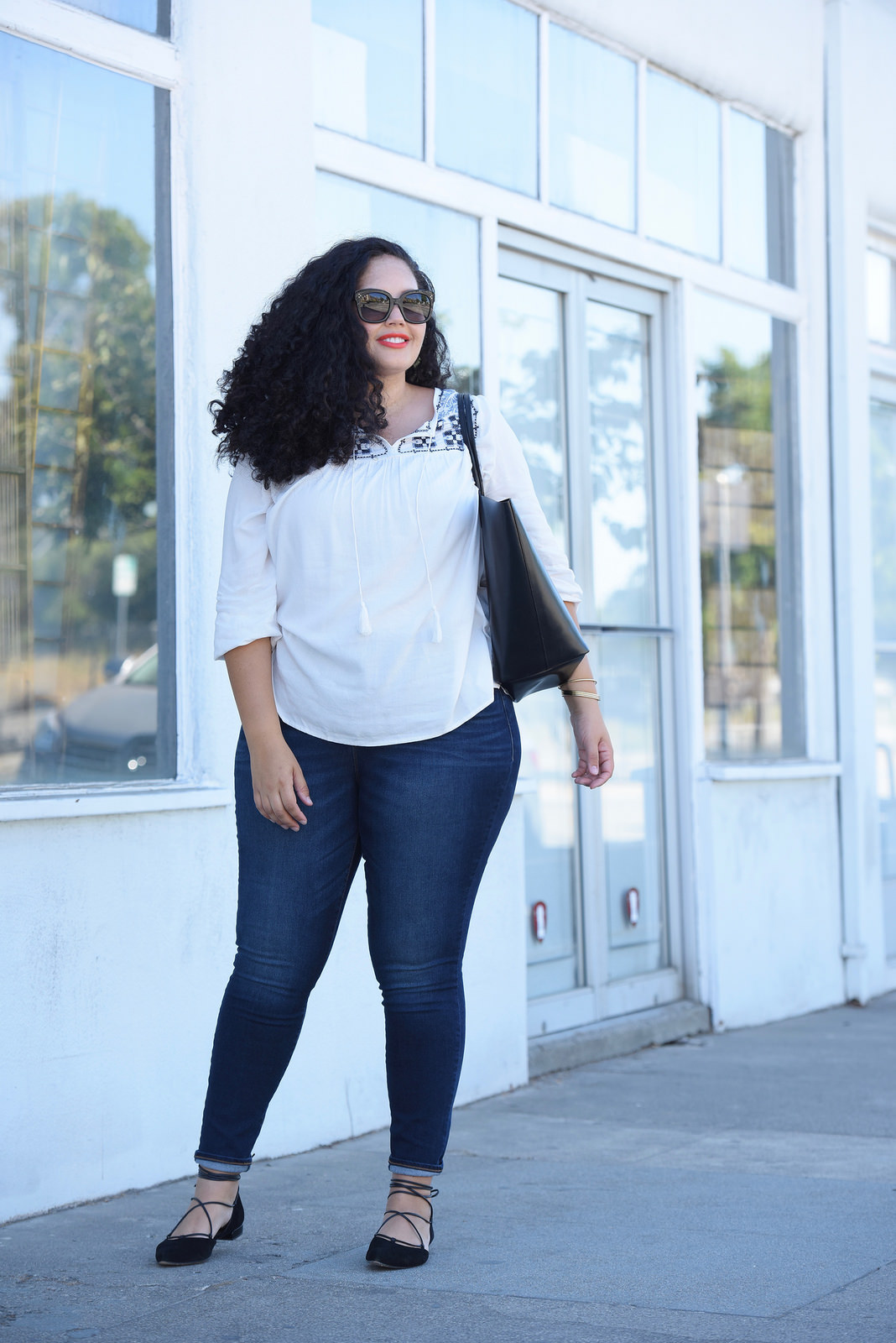 Tanesha Awasthi, also known as Girl With Curves, wearing dark wash plus size skinny jeans, a swing blouse, lace-up flats, tote bag and Celine sunglasses.
