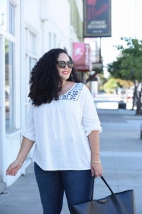 Tanesha Awasthi, also known as Girl with Curves, wearing dark wash plus size skinny jeans, a swing blouse, lace-up flats, tote bag and Celine sunglasses.