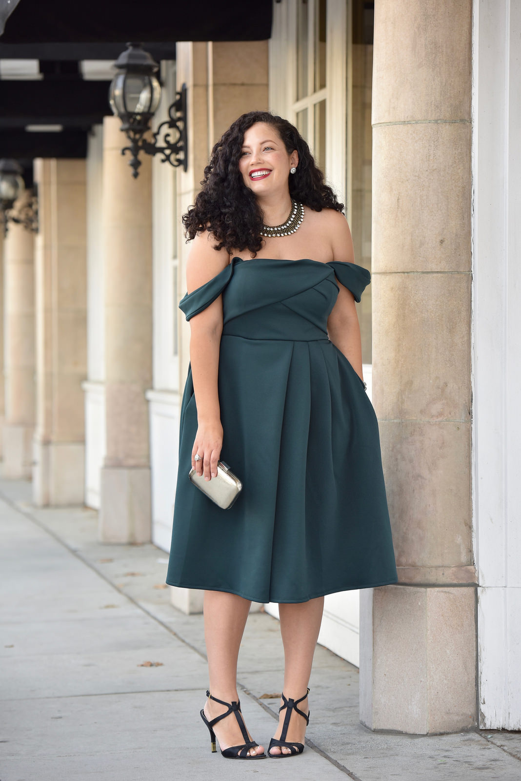 Girl With Curves blogger Tanesha Awasthi wears an emerald off-shoulder dress, silver box clutch and t-strap heels in downtown San Jose, CA.