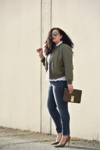 Girl With Curves blogger Tanesha Awasthi wears a satin bomber jacket, peplum top, skinny jeans, olive green pumps and vintage Louis Vuitton clutch bag.