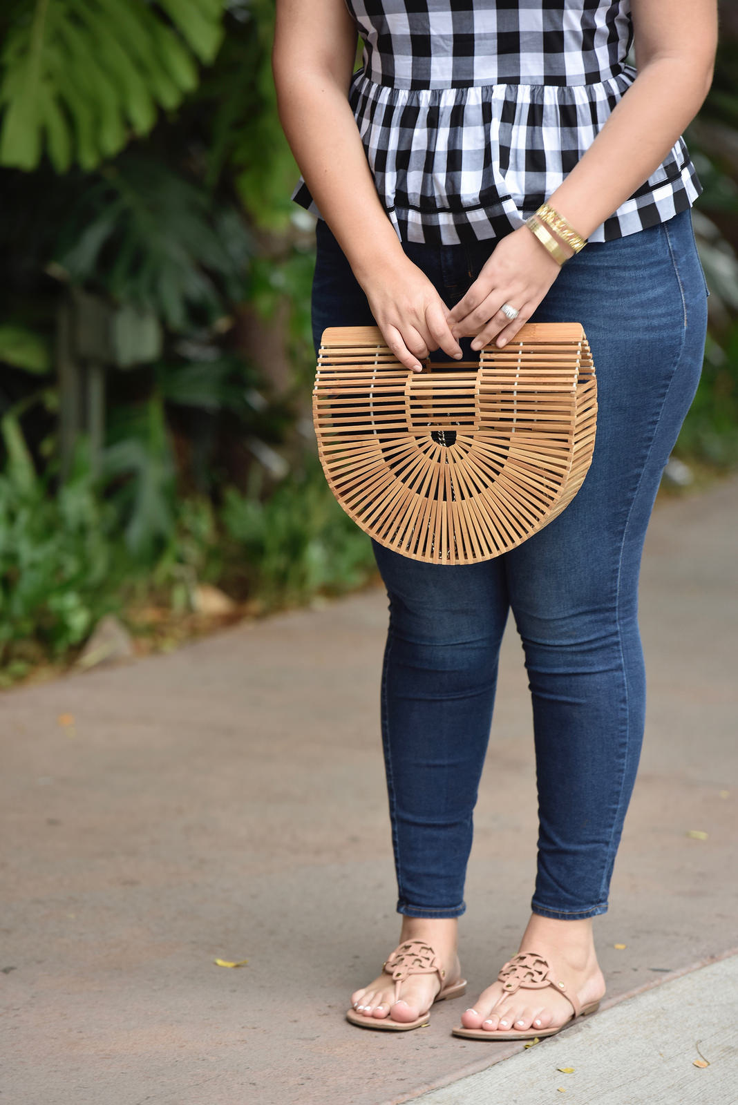 Girl With Curves blogger Tanesha Awasthi wears a gingham peplum, skinny jeans, Tory Burch Miller sandals, wicker bag and boater hat in Hawaii.
