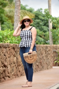 Girl With Curves blogger Tanesha Awasthi wears a gingham peplum, skinny jeans, wicker bag, Celine sunglasses, Tory Burch sandals and boater hat in Hawaii.