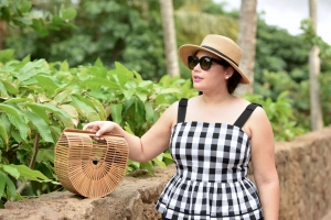 Girl With Curves blogger Tanesha Awasthi wears a gingham tank top peplum, boater hat and straw bag in Hawaii.