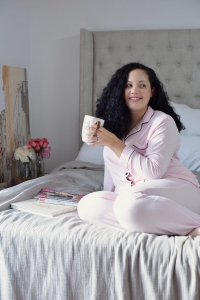 Tanesha Awasthi of Girl With Curves, lounging in Pink and Black pretty pajamas from Nordstrom on a Restoration Hardware bed.